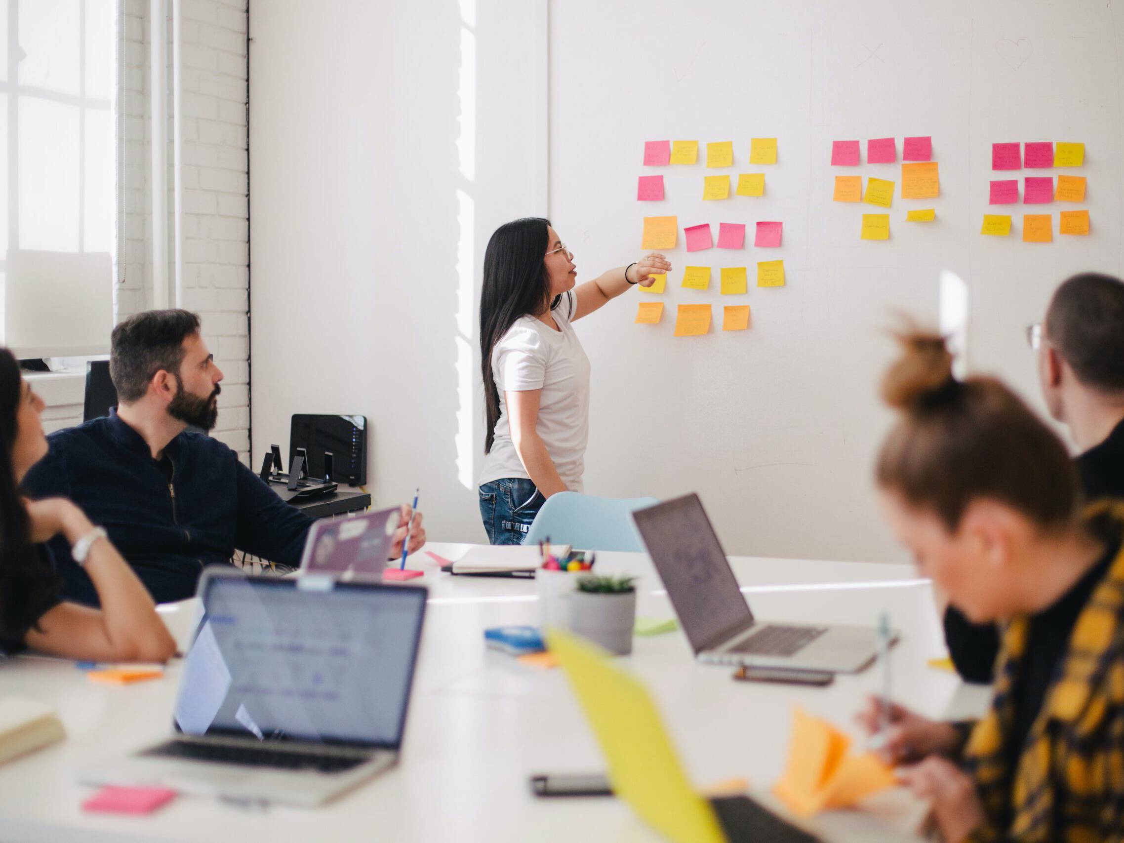 Ein heller Konferenzraum bildet eine agile Workshop-Situation ab, die wir als Transformations-Expert:innen auch genauso praktizieren: Offene MacBooks, Post-its, Marker und mehrere Fachexperte:innen an einem Tisch.